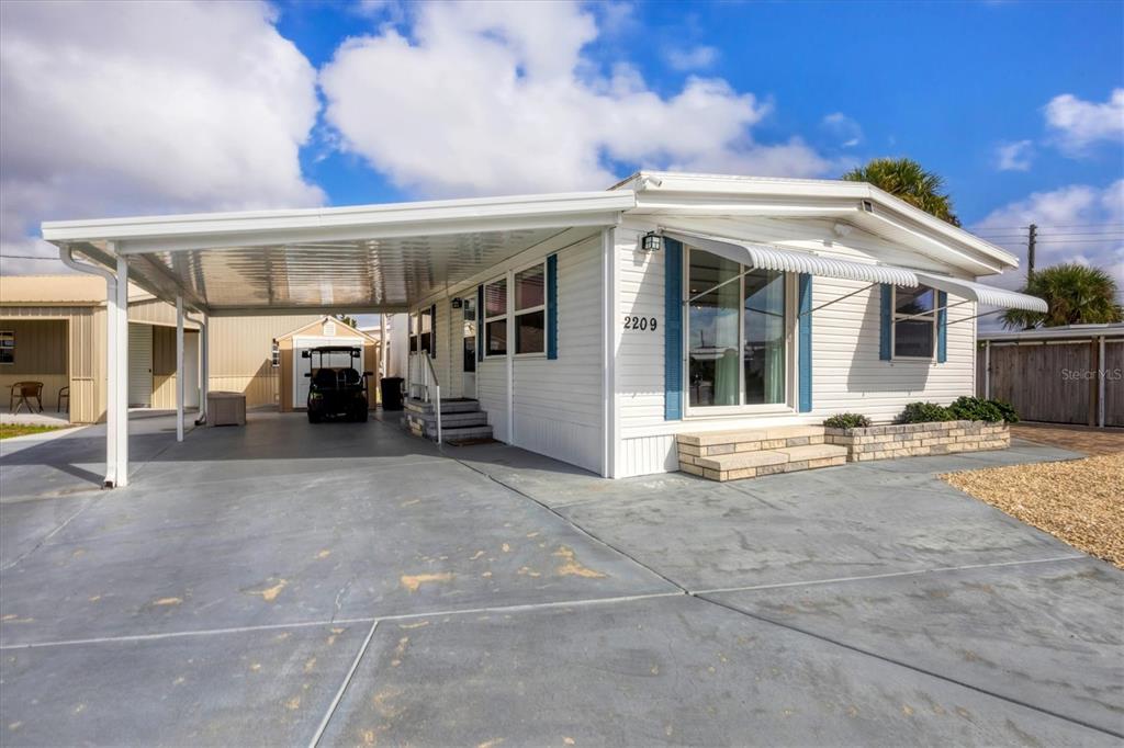 A white mobile home with blue shutters, a large carport, and a concrete driveway — 2209 IOWA AVENUE, BRADENTON, FL