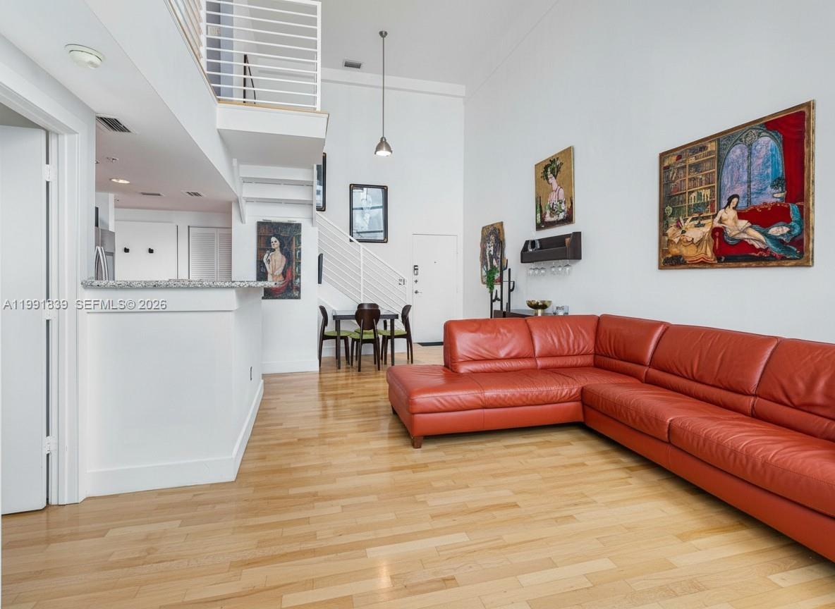 A living room features a red sectional sofa, hardwood floors, and a staircase to a loft — 7728 Collins Ave # 16, Miami Beach FL 33141, MIAMI BEACH, FL