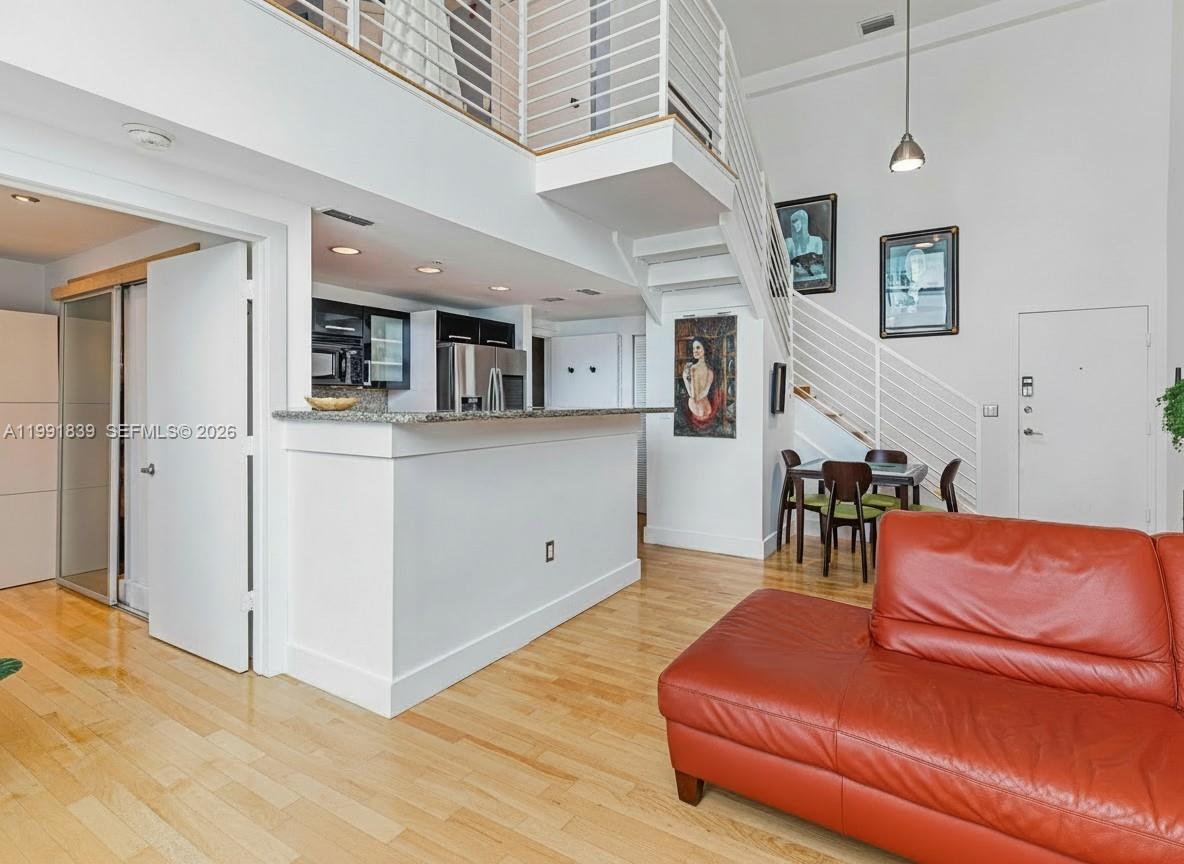 A living room with a red leather sofa, kitchen counter, and staircase to a loft — 7728 Collins Ave # 16, Miami Beach FL 33141, MIAMI BEACH, FL