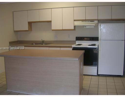 A kitchen features light wood cabinets, a central island, white appliances, and tiled flooring — 4055 W Mcnab Rd # H303, Pompano Beach FL 33069, POMPANO BEACH, FL