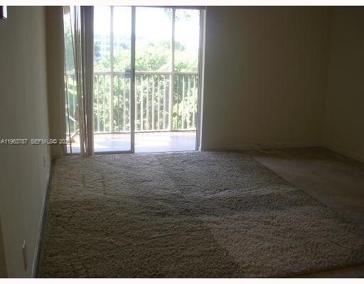 A carpeted living room features a sliding glass door leading to a screened-in balcony — 4055 W Mcnab Rd # H303, Pompano Beach FL 33069, POMPANO BEACH, FL