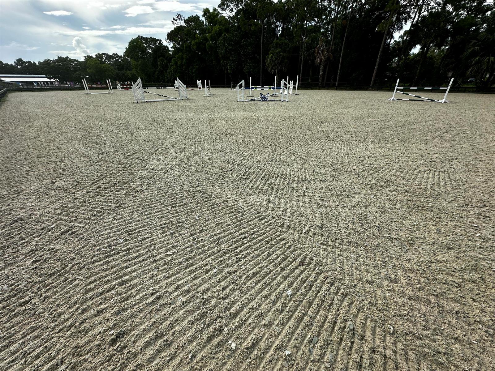 An outdoor equestrian riding arena features several show jumping obstacles set on a groomed sand surface — 13009 Collecting Canal Road, FL 33470, FL