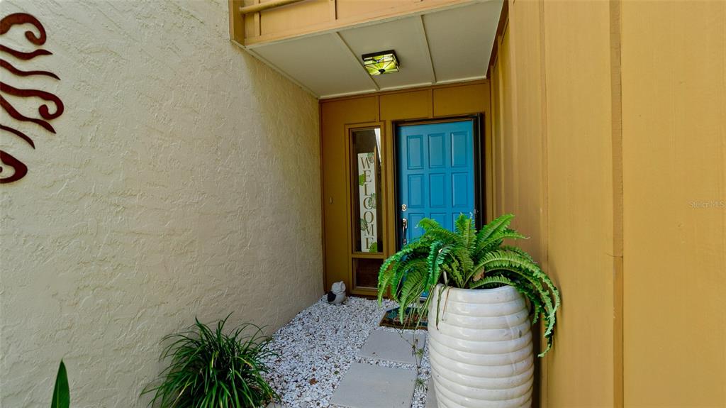 A bright blue front door is set in a recessed entryway with a stone-covered floor — 2407 QUAIL COURT, BRADENTON, FL