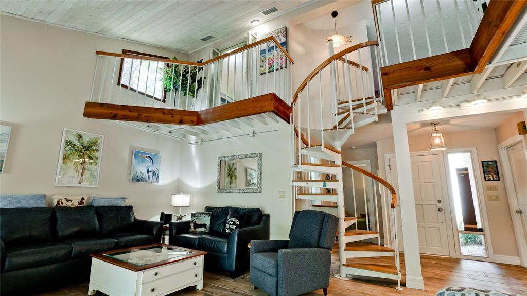 A living room features a spiral staircase, a lofted walkway, and black leather sofas — 2407 QUAIL COURT, BRADENTON, FL