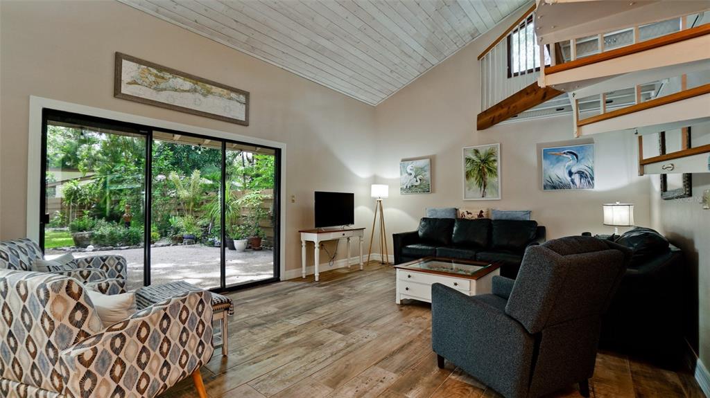 A living room features a vaulted ceiling, wood-look tile floors, and a spiral staircase — 2407 QUAIL COURT, BRADENTON, FL