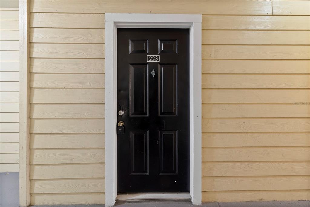A black front door with the number 223 is set into light yellow horizontal siding — 2648 ROBERT TRENT JONES DRIVE UNIT 223, ORLANDO, FL