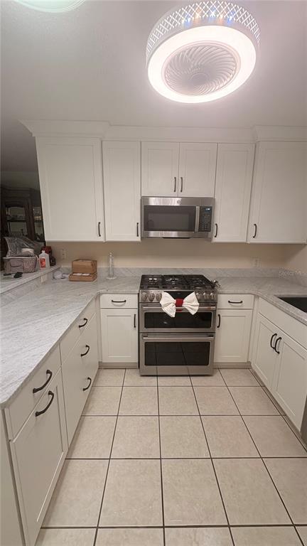 A kitchen features white cabinets, stainless steel appliances, and light-colored countertops with tile flooring — 773 ARTESIA AVENUE, THE VILLAGES, FL