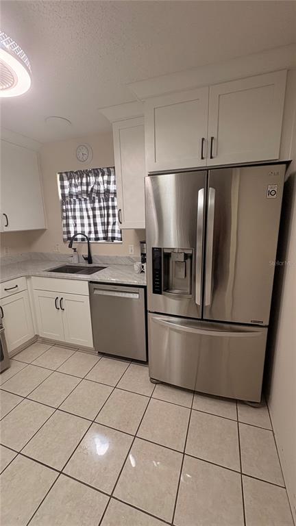 A kitchen features white cabinets, stainless steel appliances, a tiled floor, and a window with curtains — 773 ARTESIA AVENUE, THE VILLAGES, FL