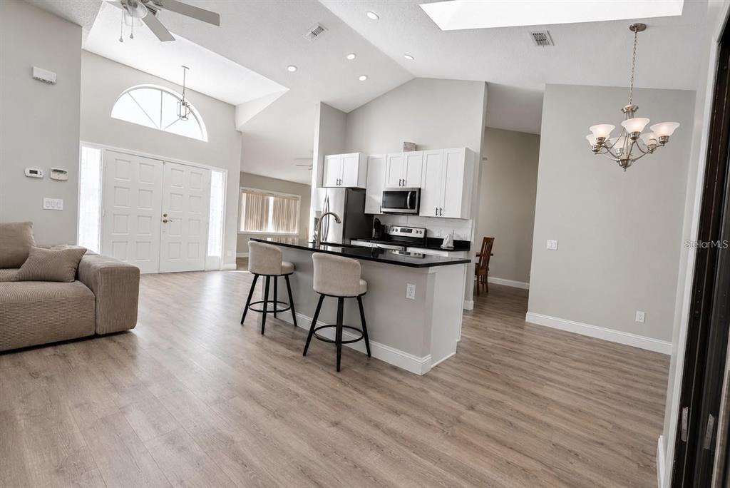 An open-concept living area features a kitchen with white cabinets, black countertops, and wood flooring — 10 FALLS PLACE, PALM COAST, FL