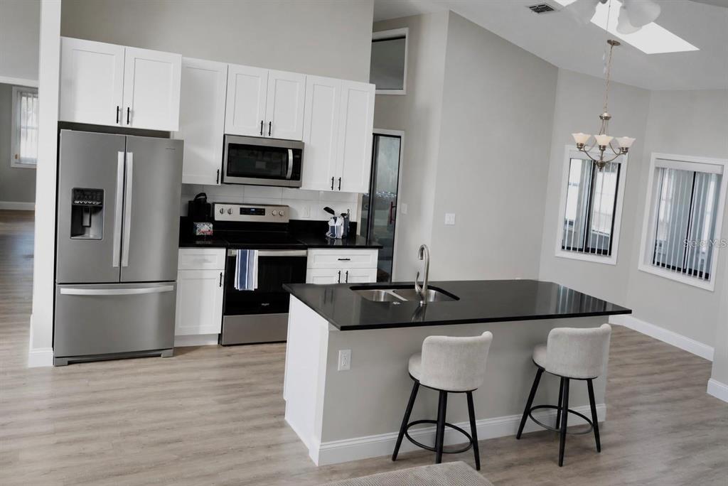 A kitchen features white cabinets, stainless steel appliances, a black island, and light wood flooring — 10 FALLS PLACE, PALM COAST, FL