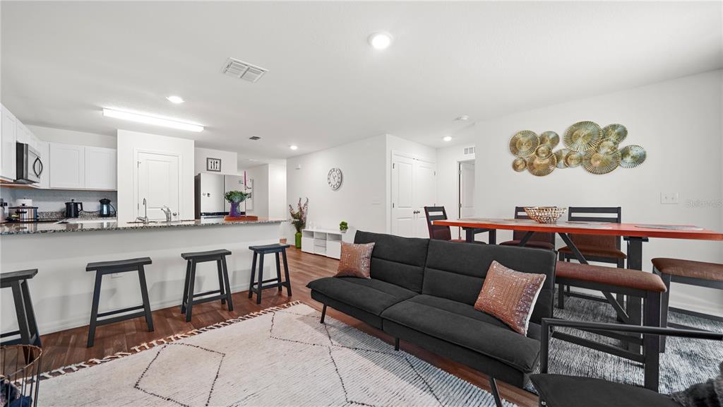 An open-concept living and dining area features a kitchen island, dark sofa, and wood flooring — 4236 GARBETT TERRACE, NORTH PORT, FL