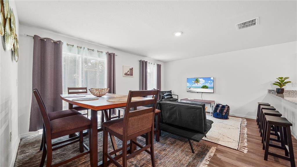 An open-concept living and dining area features dark wood furniture, a wall-mounted television, and bar seating — 4236 GARBETT TERRACE, NORTH PORT, FL