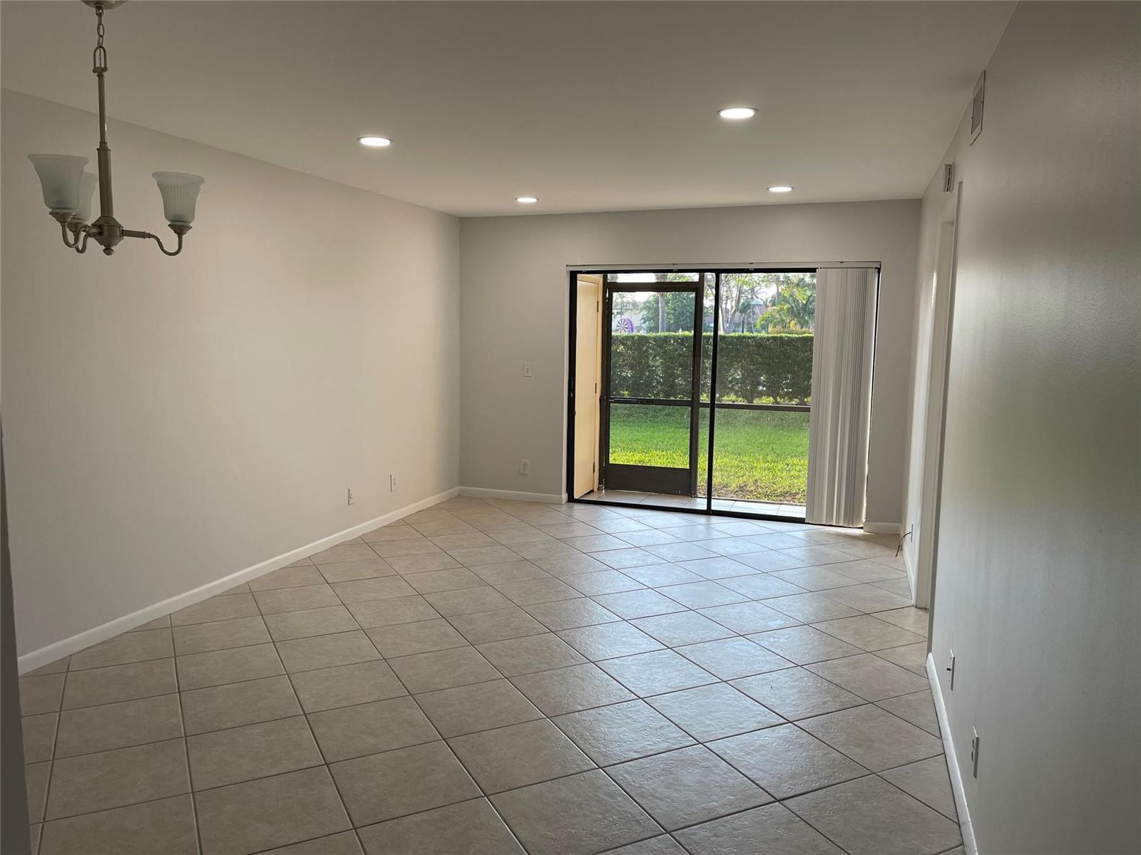 An empty room with light-colored tile floors, recessed lighting, a chandelier, and a sliding glass door — 6549 Somerset Drive # 106, Boca Raton FL 33433, BOCA RATON, FL