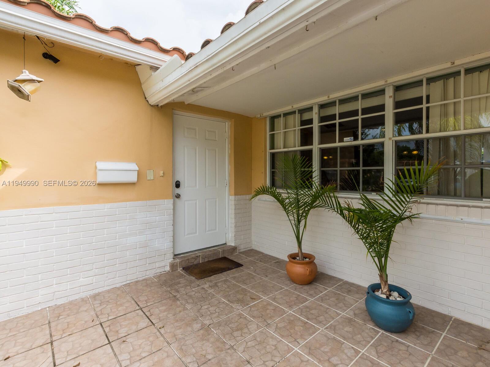 A tiled front porch features a white door, two potted palm plants, and brick siding — 5524 Garfield St, Hollywood FL 33021, HOLLYWOOD, FL