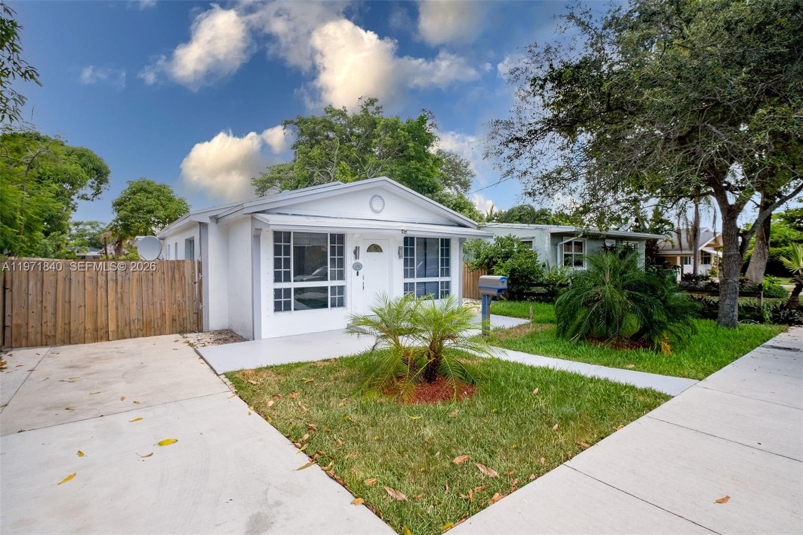 A white single-story house features a front lawn, a concrete driveway, and a wooden fence — 132 SW 2nd Ave, Hallandale Beach FL 33009, HALLANDALE BEACH, FL