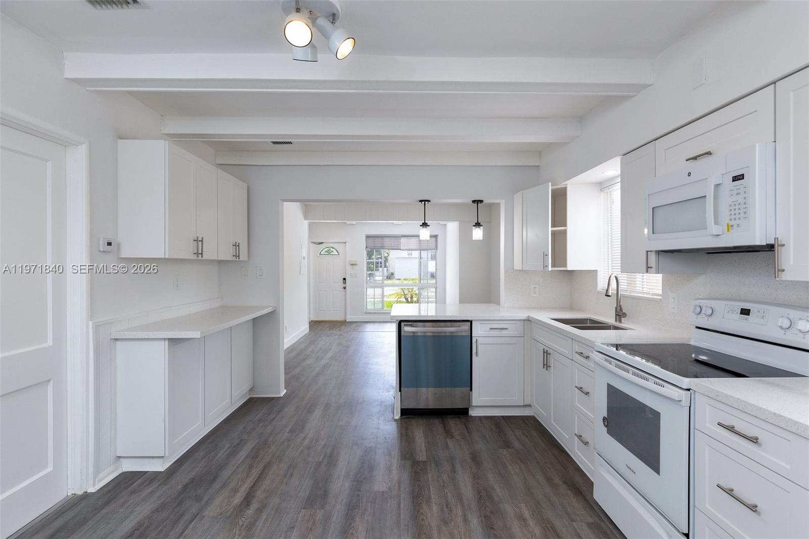 A bright kitchen features white cabinetry, stainless steel appliances, and dark wood-look flooring — 132 SW 2nd Ave, Hallandale Beach FL 33009, HALLANDALE BEACH, FL