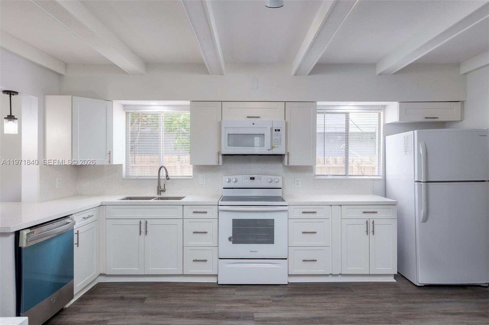 A white kitchen features shaker cabinets, stainless steel appliances, and wood-look flooring — 132 SW 2nd Ave, Hallandale Beach FL 33009, HALLANDALE BEACH, FL