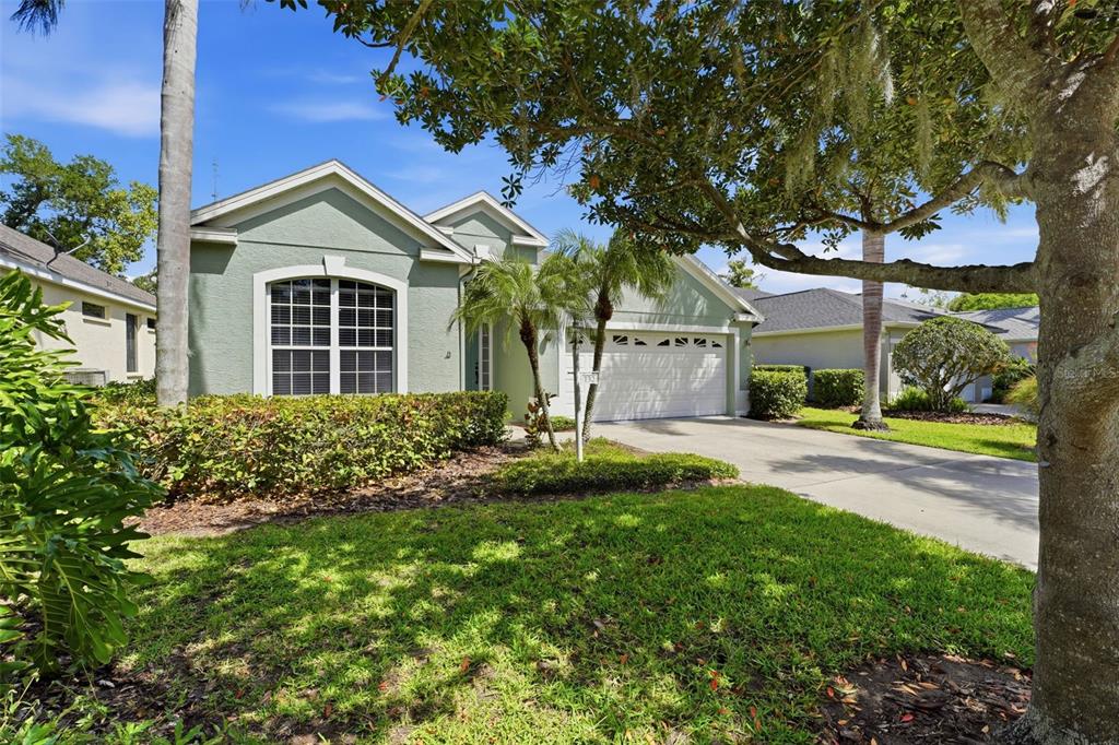 A single-story house with light green stucco siding, a two-car garage, and a front lawn — 132 TALL TREES COURT, SARASOTA, FL