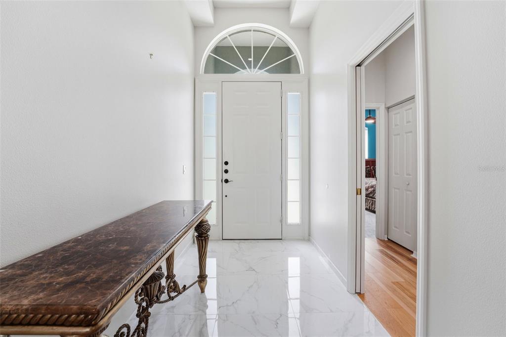 A bright entryway features white marble floors, a decorative console table, and a glass-paneled door — 132 TALL TREES COURT, SARASOTA, FL