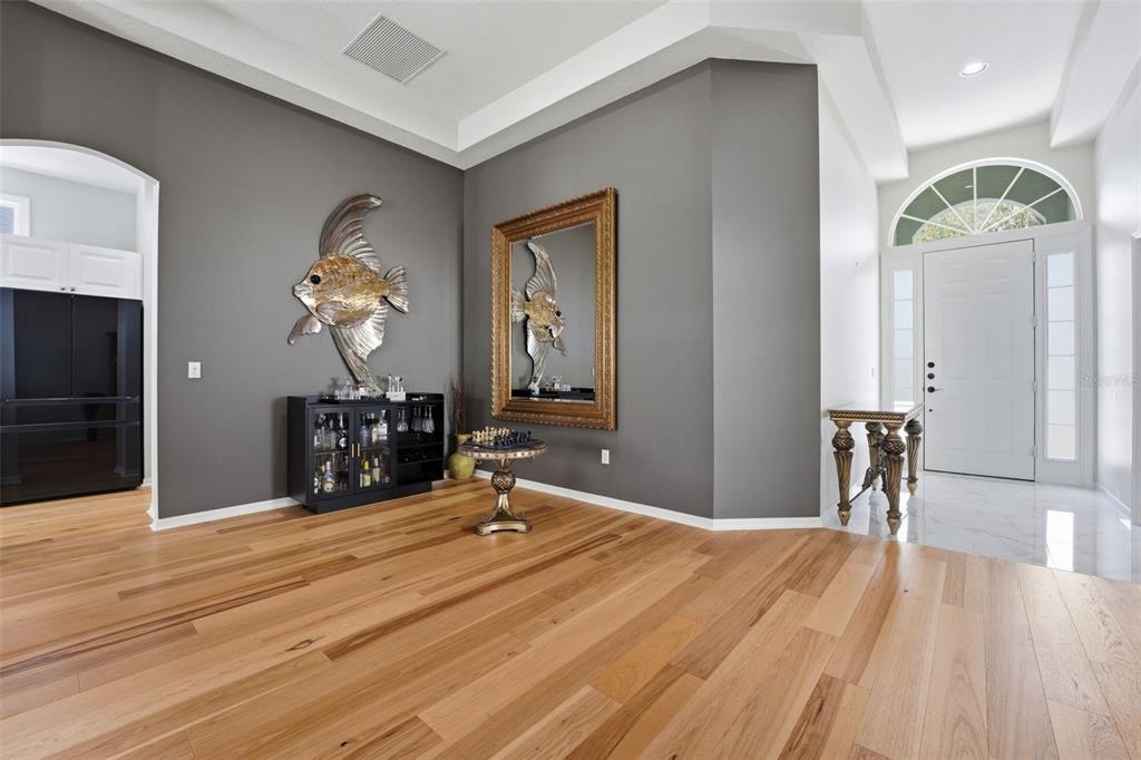 A foyer with light wood flooring, gray walls, a bar cabinet, and a large gold mirror — 132 TALL TREES COURT, SARASOTA, FL