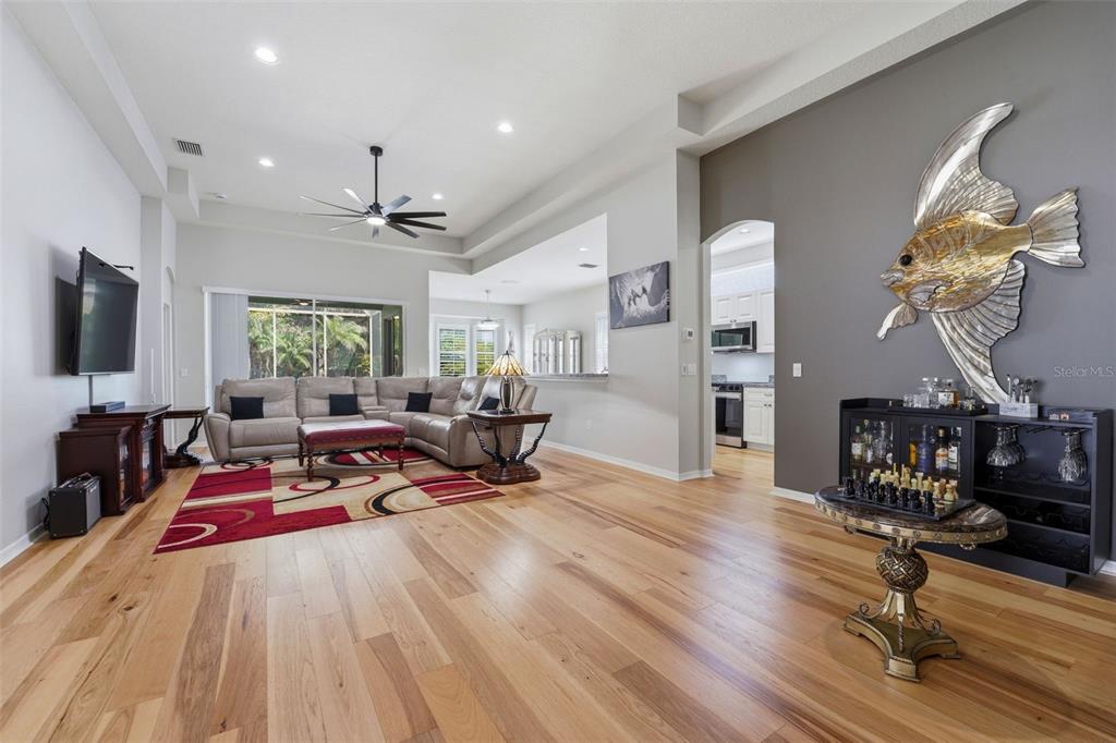 A living room features hardwood floors, a sectional sofa, a red rug, and wall art — 132 TALL TREES COURT, SARASOTA, FL