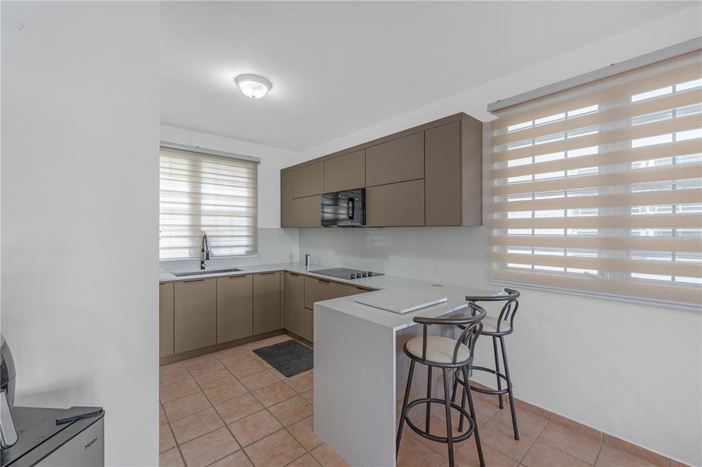 A modern kitchen features taupe cabinetry, light countertops, a breakfast bar, and tile flooring — SR 307 km 7.4 COND PASEO DEL MAR BOQUERON WARD UNIT 104, BOQUERON, PR