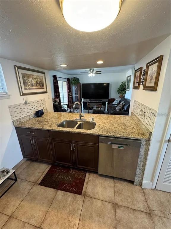 A kitchen features granite countertops, dark wood cabinets, a stainless steel dishwasher, and tile flooring — 1836 WARRINGWOOD DRIVE UNIT B4, ORLANDO, FL