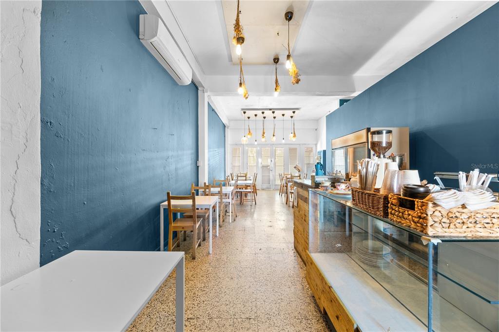 A narrow cafe interior features blue walls, a glass display counter, and wooden tables — 311 MENDEZ VIGO, DORADO, PR