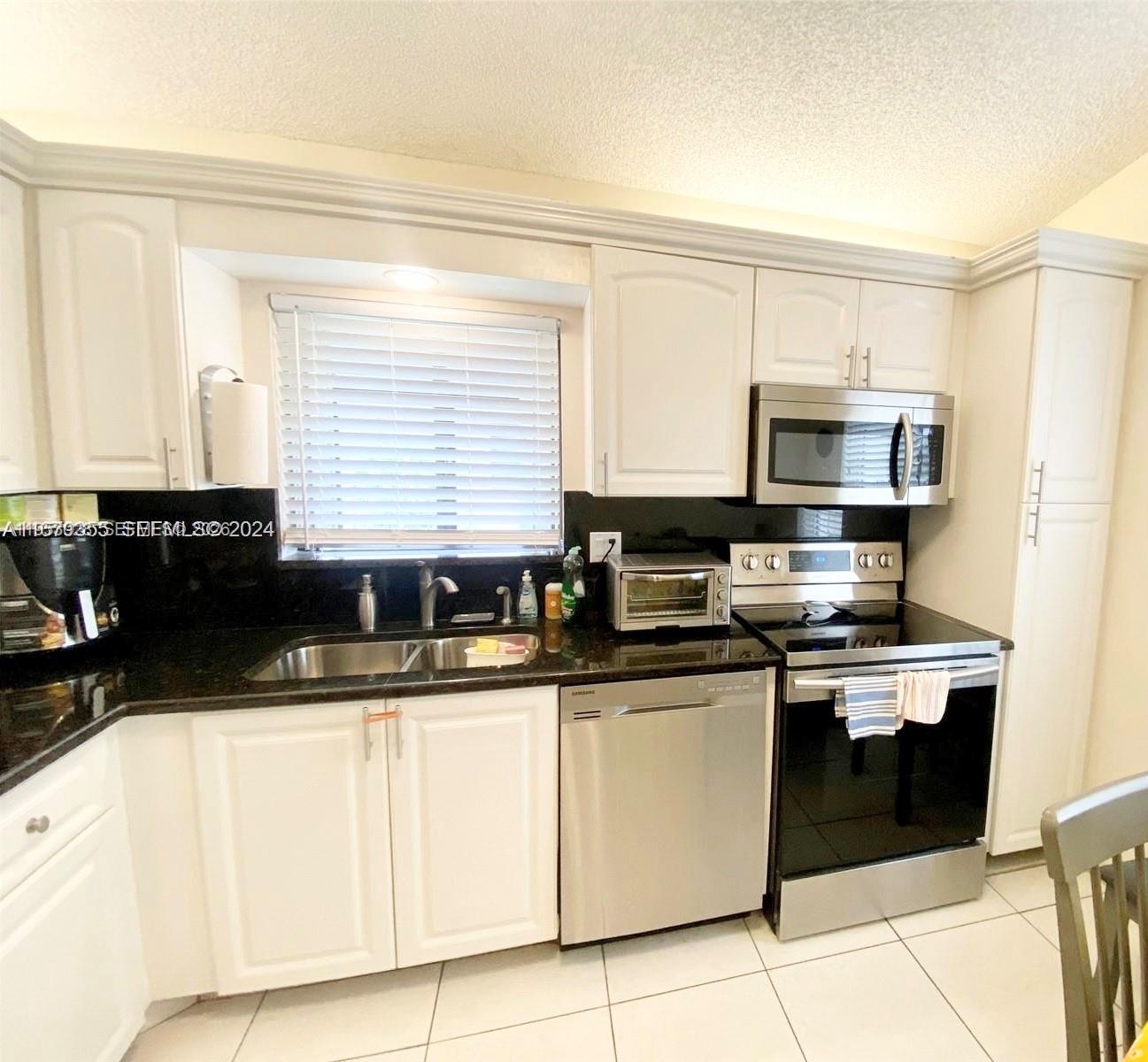 A kitchen features white cabinets, black countertops, stainless steel appliances, and a window above the sink — 8089 Sweetbriar Way, Boca Raton FL 33496, BOCA RATON, FL