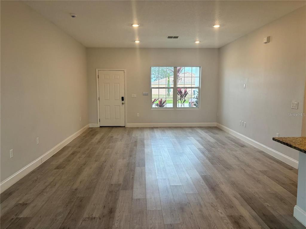 An empty living room features light wood-look flooring, recessed lighting, and a front entry door — 423 CHURCHILL COURT, KISSIMMEE, FL