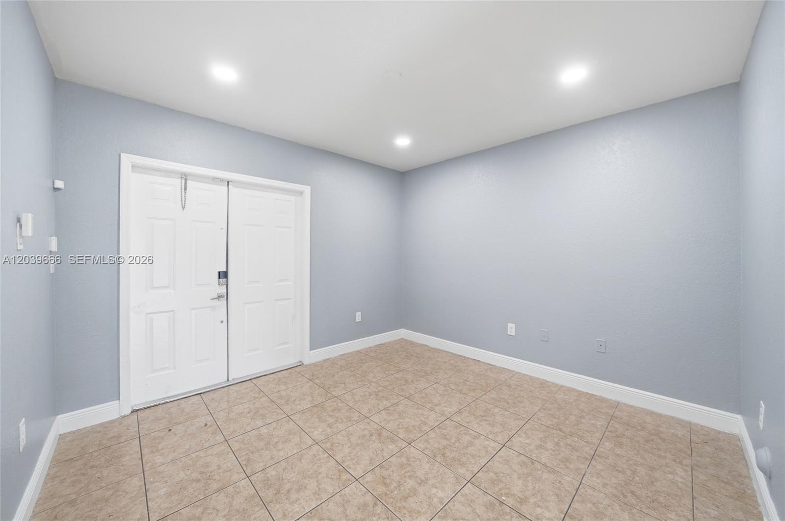 An empty room features light blue walls, tile flooring, recessed lighting, and double entry doors — FLORIDA CITY, FL