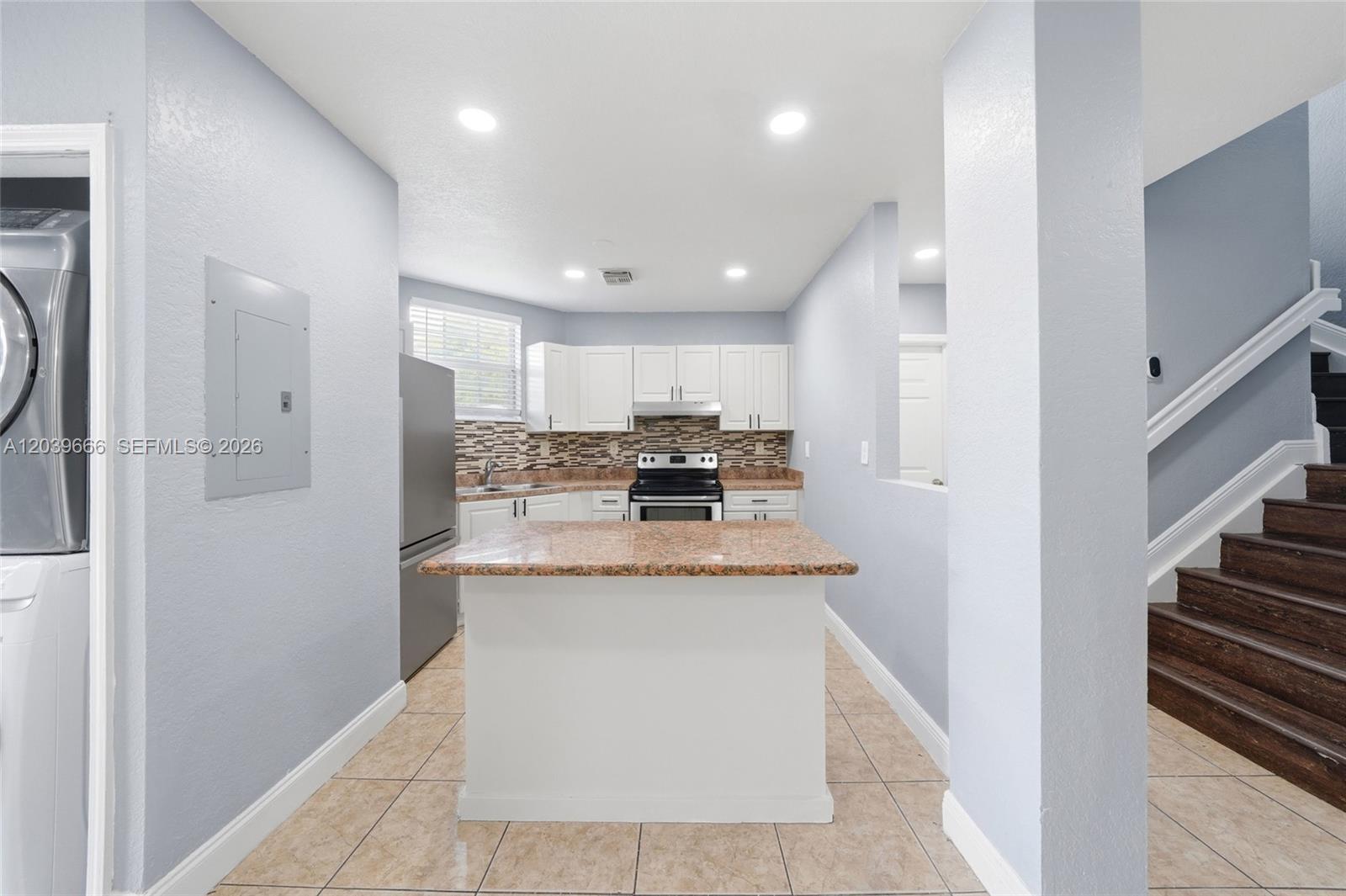 A kitchen features white cabinets, granite countertops, a central island, and adjacent wooden stairs — FLORIDA CITY, FL