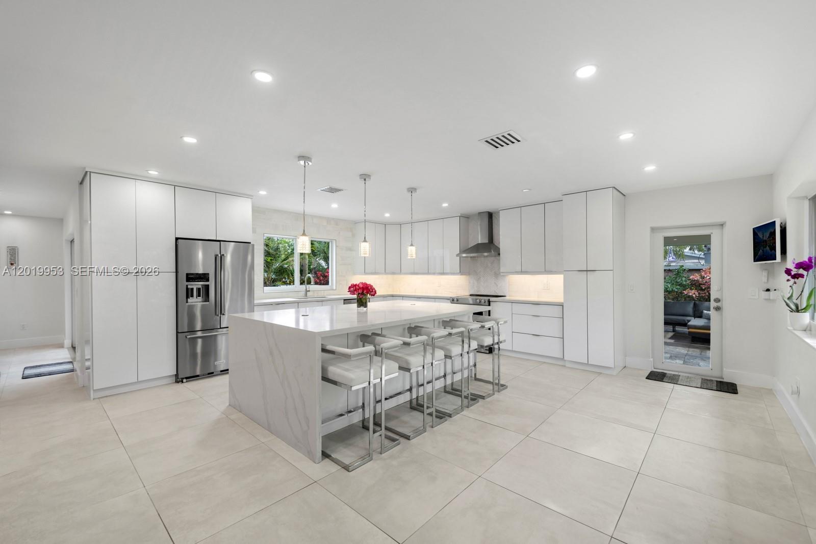 A modern white kitchen features a large marble-topped island with four stools and tile flooring — 600 NE 4th St, Pompano Beach FL 33060, POMPANO BEACH, FL