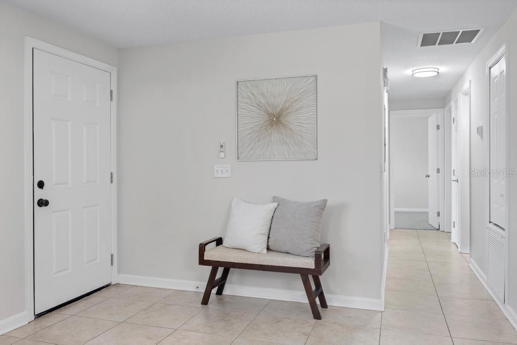 A tiled entryway features a white door, a wooden bench with two pillows, and wall art — 8149 JUSTIN ROAD S, JACKSONVILLE, FL