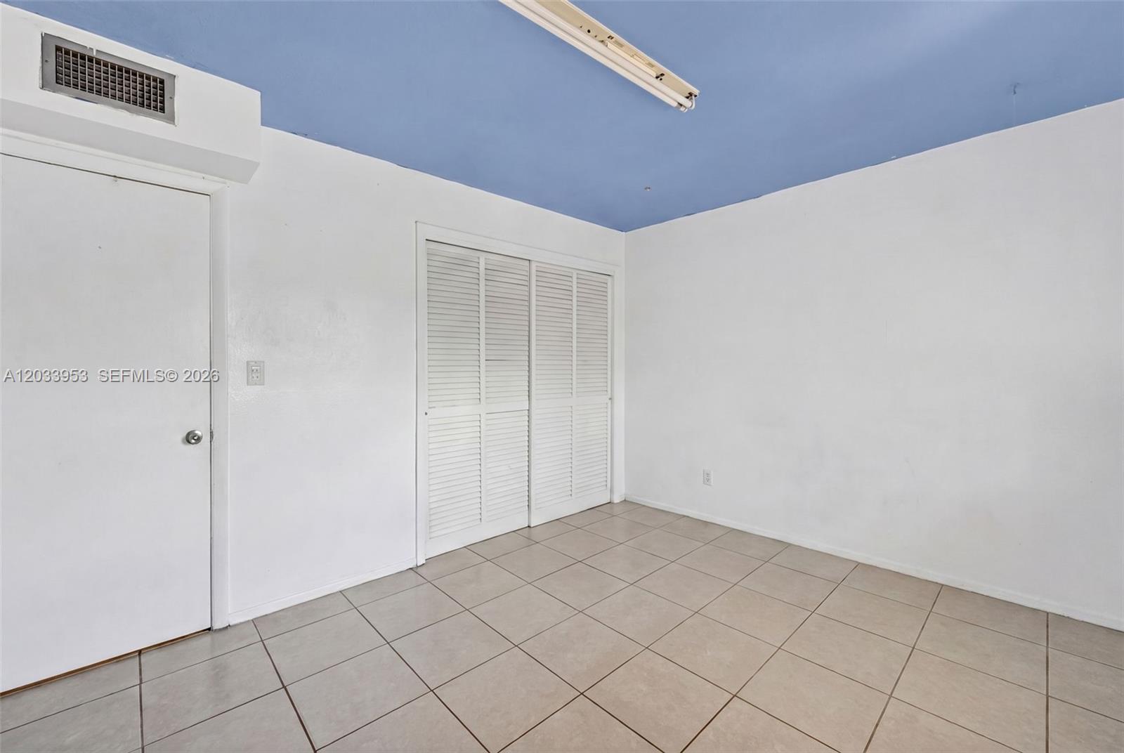 A room with white walls, a blue ceiling, tile flooring, and louvered closet doors — 1540 NE 191st St # 145, Miami FL 33179, MIAMI, FL