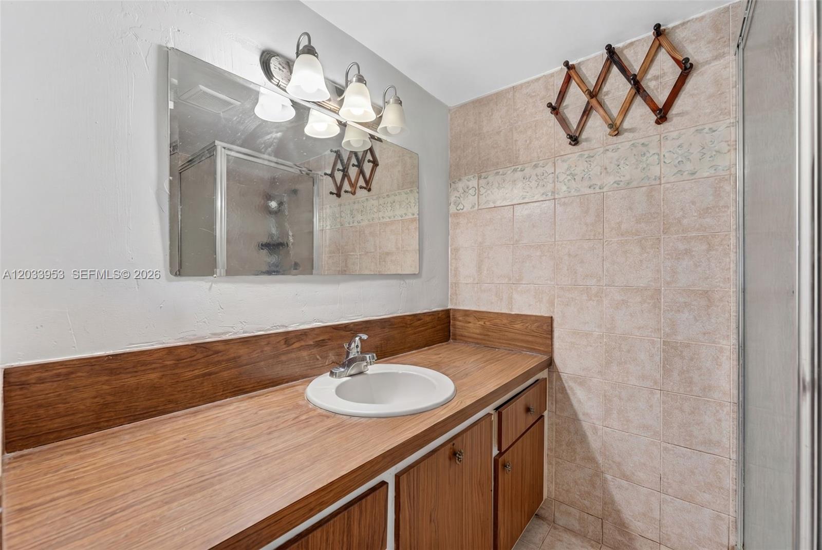 A bathroom features a wood vanity, a white sink, a mirror, and tiled walls — 1540 NE 191st St # 145, Miami FL 33179, MIAMI, FL