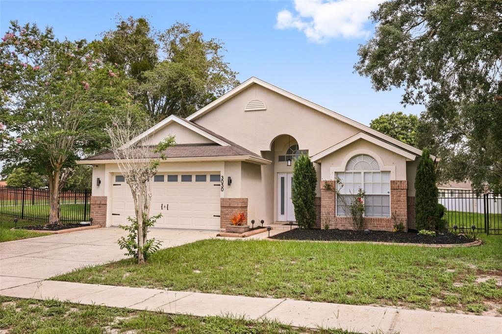 A single-story house with a beige stucco exterior, a two-car garage, and a front lawn — 3050 MOUNTEL AVENUE, DELTONA, FL