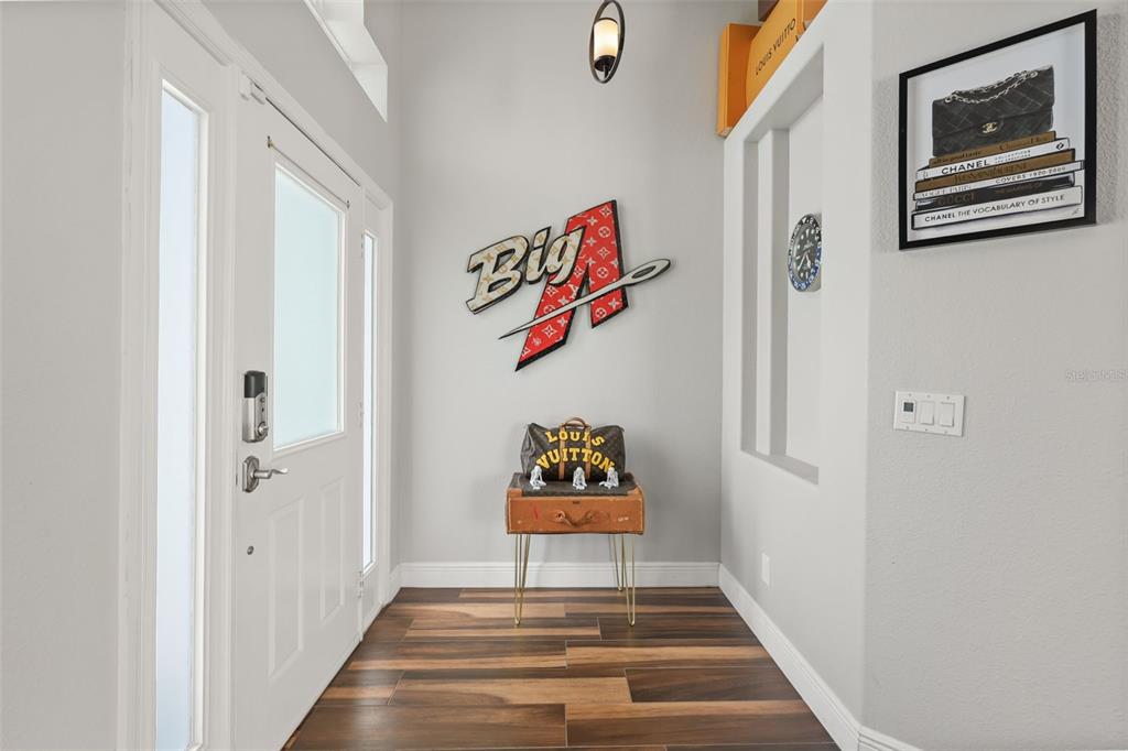 A modern entryway features wood-look tile flooring, a designer-themed wall display, and a front door — 3050 MOUNTEL AVENUE, DELTONA, FL