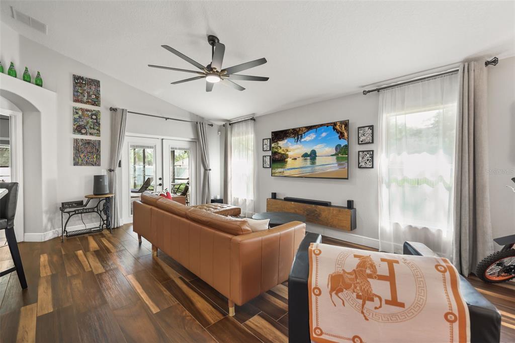 A living room features a tan leather sofa, a wall-mounted television, and wood-look tile flooring — 3050 MOUNTEL AVENUE, DELTONA, FL