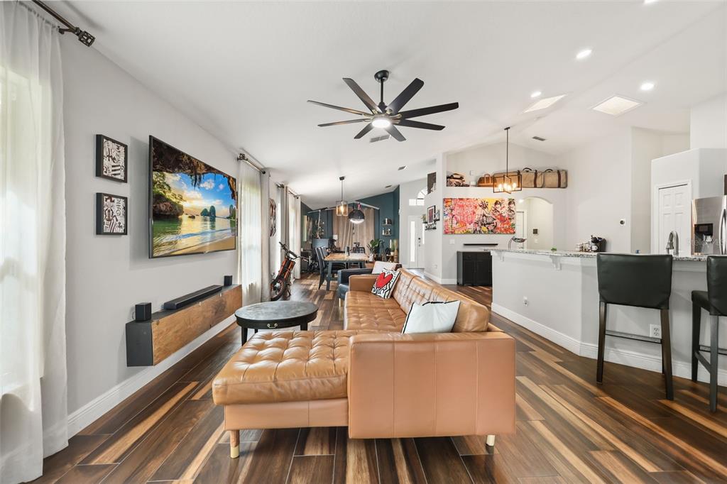 A living room features a tan leather sectional, wood-look tile floors, and a wall-mounted television — 3050 MOUNTEL AVENUE, DELTONA, FL