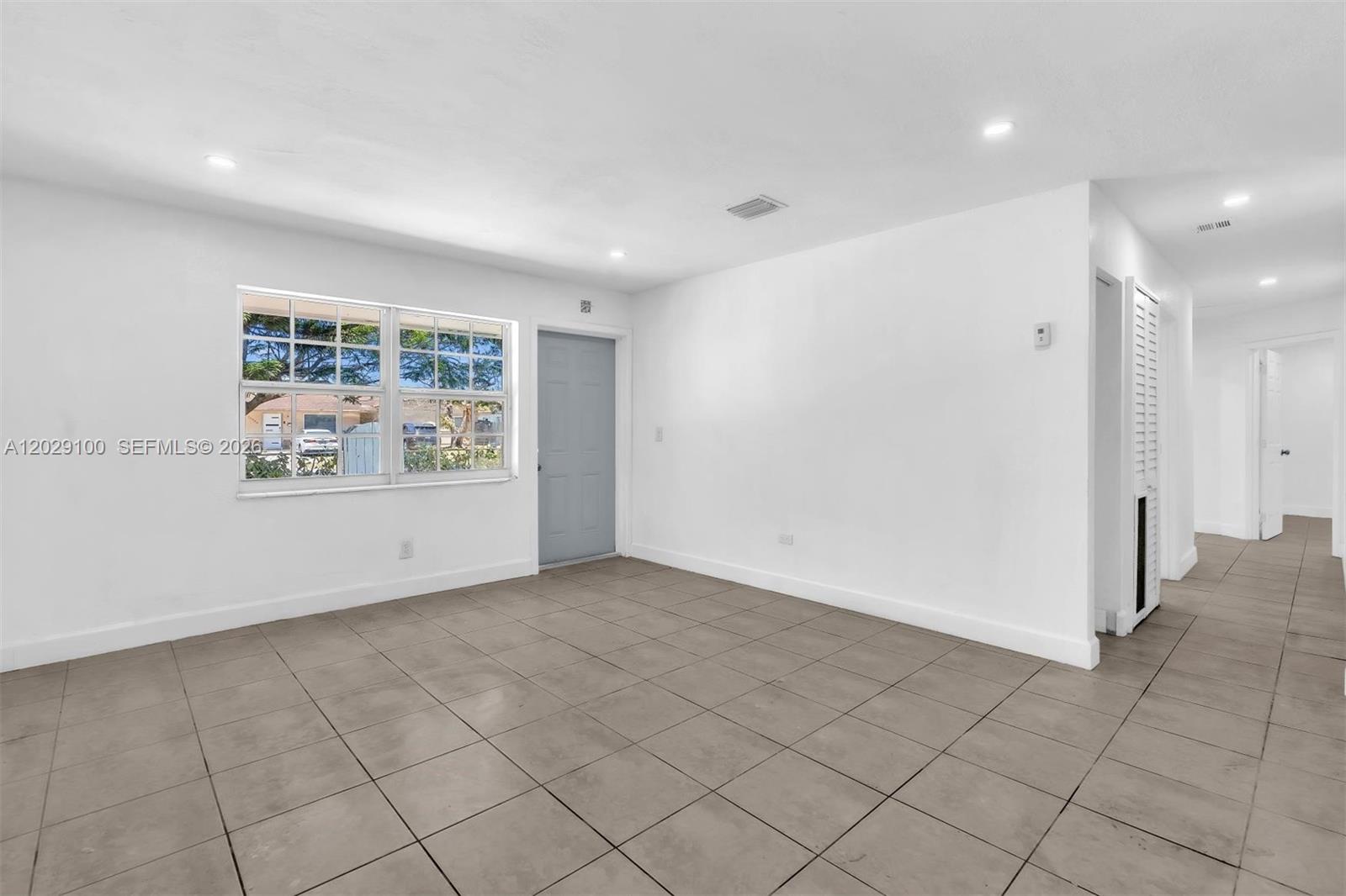 An empty room features white walls, light-colored tile flooring, a window, and a gray door — 11790 SW 34th St, Miami FL 33175, MIAMI, FL