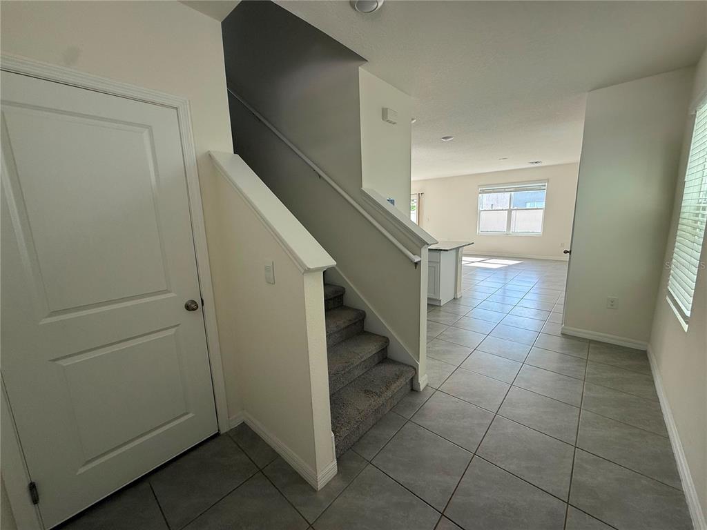 An entryway features a carpeted staircase, tile flooring, and a view into the living area — 2763 COMMON FIG RUN, WESLEY CHAPEL, FL