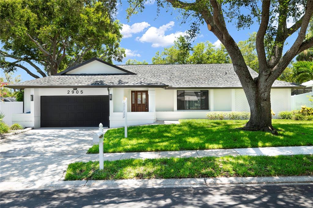 A single-story house with a white exterior, dark garage door, and a large front tree — 2905 BLUFFS DRIVE, LARGO, FL