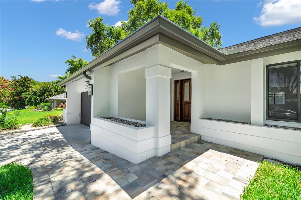 A white house exterior features a stone-paved entryway, a wooden front door, and a garage — 2905 BLUFFS DRIVE, LARGO, FL
