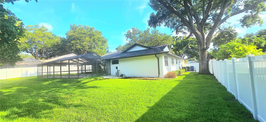 The backyard features a white house with a screened-in pool enclosure and a vinyl fence — 2905 BLUFFS DRIVE, LARGO, FL