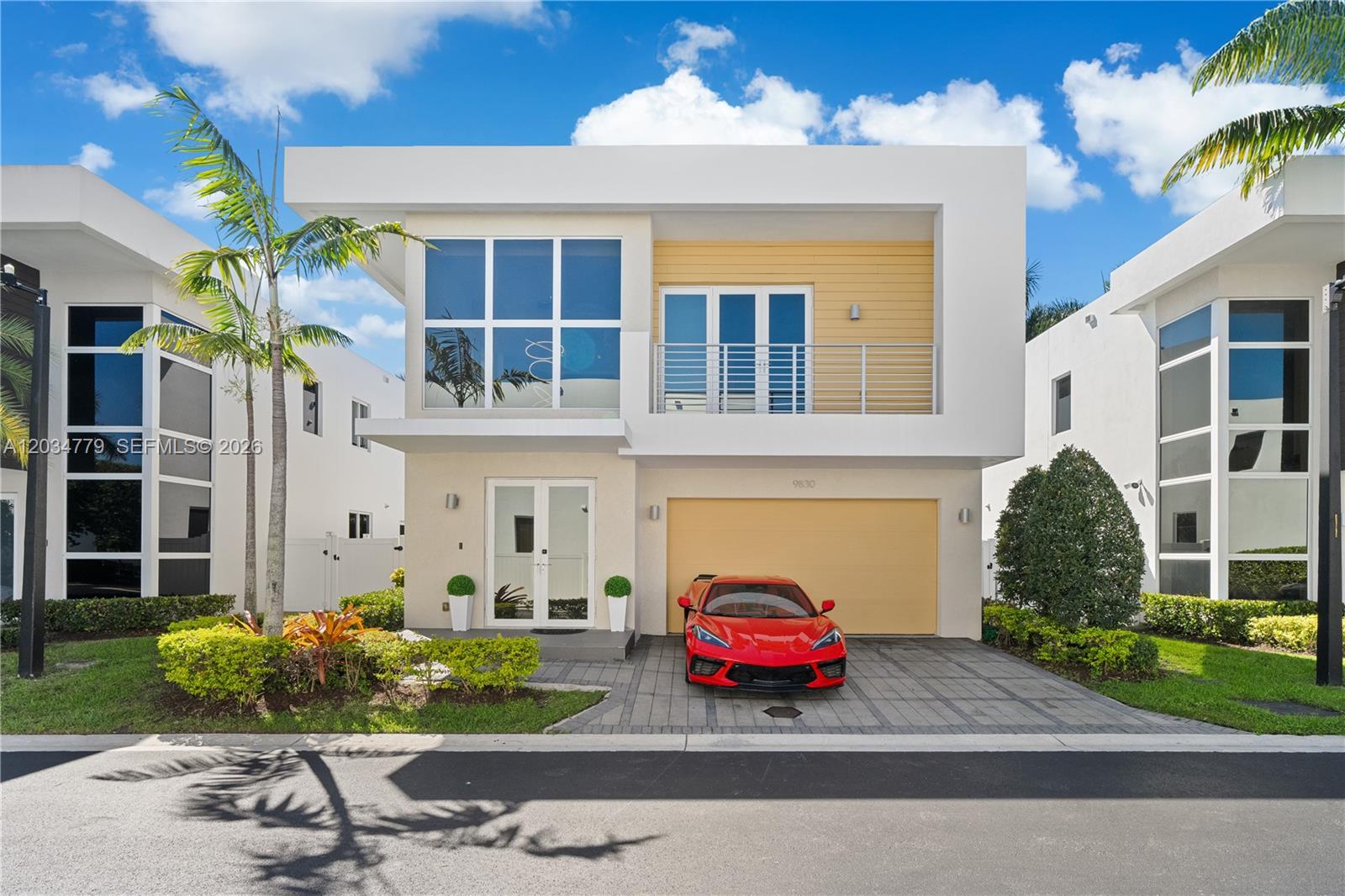 A modern two-story house features a yellow garage door, a red sports car, and balconies — 9830 NW 74th Ter, Doral FL 33178, DORAL, FL