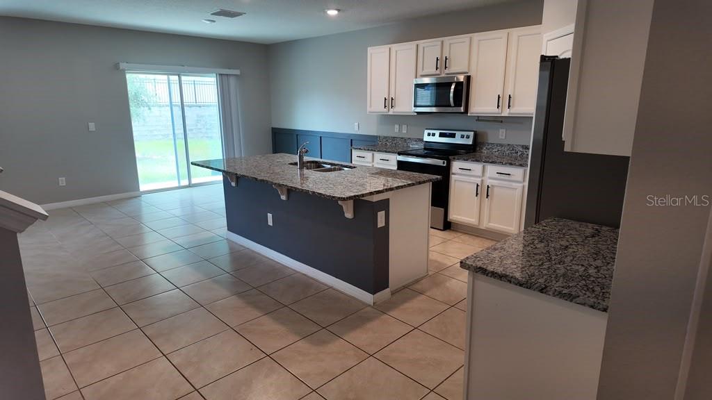 A kitchen features white cabinets, granite countertops, a center island, and tile flooring — 11237 AMBER RIDGE DRIVE, ZELLWOOD, FL