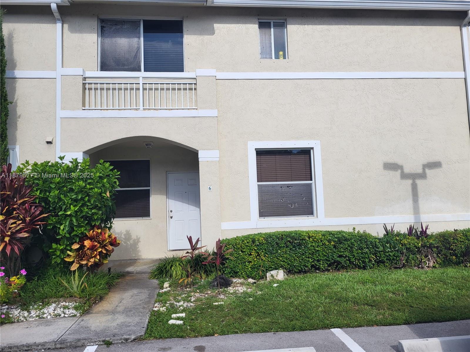 The exterior of a two-story beige townhouse features a white front door and balcony — 820 NE 212th Ter # 6, Miami FL 33179, MIAMI, FL