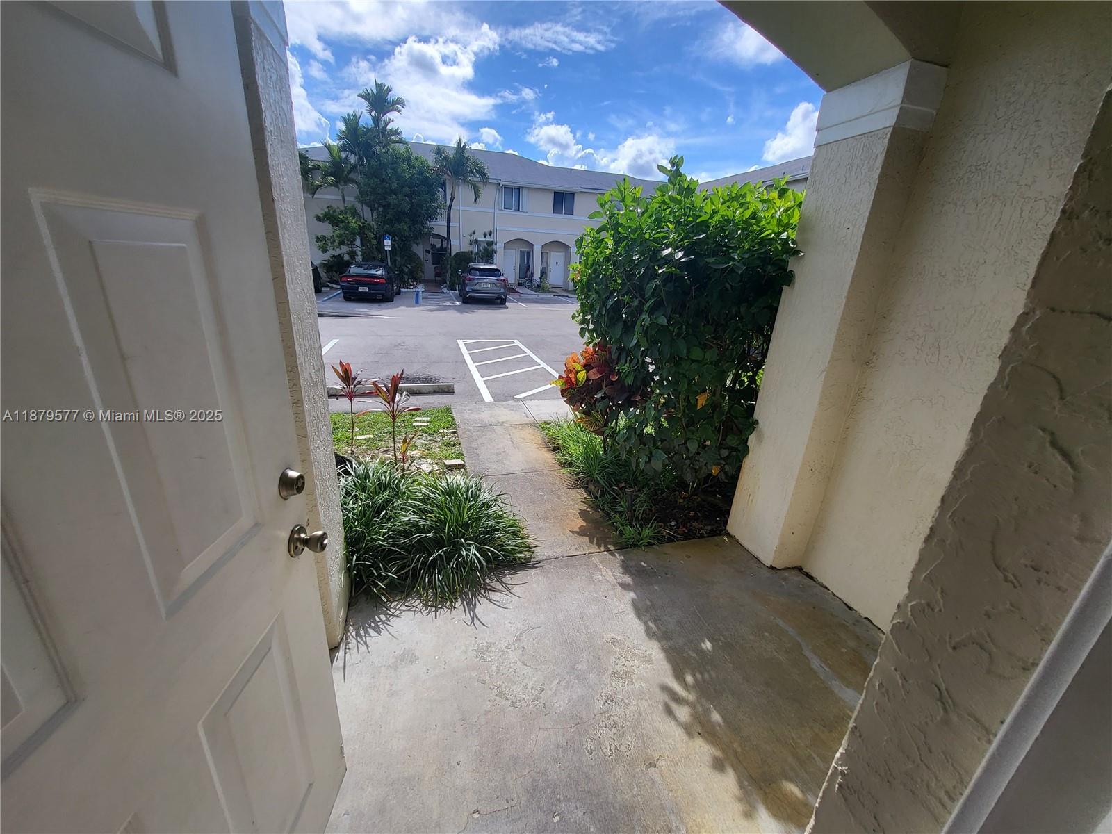 An open door reveals a concrete entryway leading to a parking lot and apartment buildings — 820 NE 212th Ter # 6, Miami FL 33179, MIAMI, FL