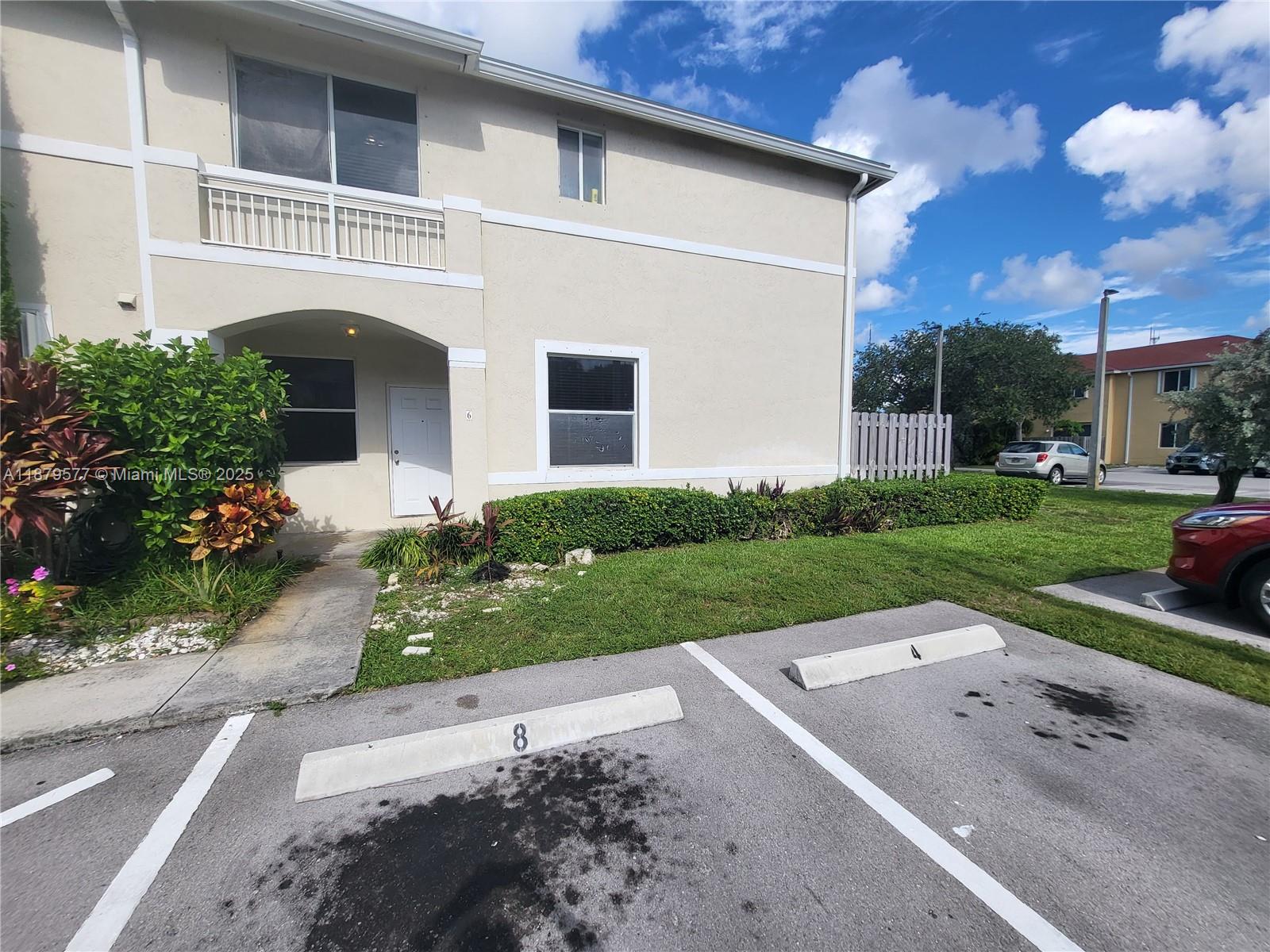 An exterior view of a two-story beige townhouse with assigned parking spaces in front — 820 NE 212th Ter # 6, Miami FL 33179, MIAMI, FL